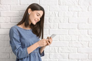 Beyaz tuğlalı arka planda cep telefonu olan güzel bir kadın.