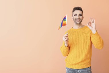 Portrait of young transgender woman with flag of LGBT showing OK gesture on color background clipart
