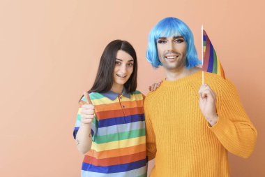 LGBT bayrağı taşıyan genç transseksüel çiftin portresi, arka planda baş parmak hareketini gösteriyor