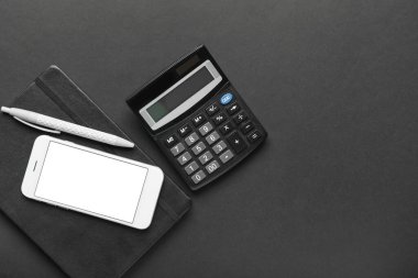 Koyu arkaplanda cep telefonu ve kırtasiye malzemesi olan hesap makinesi