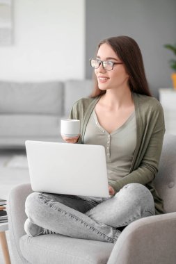 Güzel genç bayan dizüstü bilgisayarda çalışıyor ve evde kahve içiyor.