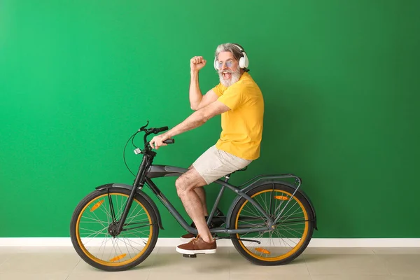カラーウォールの近くに自転車やヘッドフォンを持つ幸せな高齢者 — ストック写真