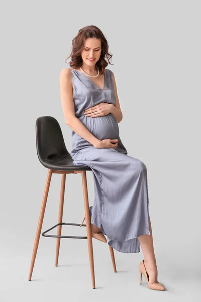 美しい妊娠中の女性座っています上の椅子に灰色の背景 — ストック写真
