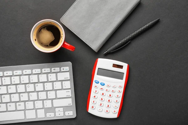 Calculator with stationery and computer keyboard and cup of coffee on dark background