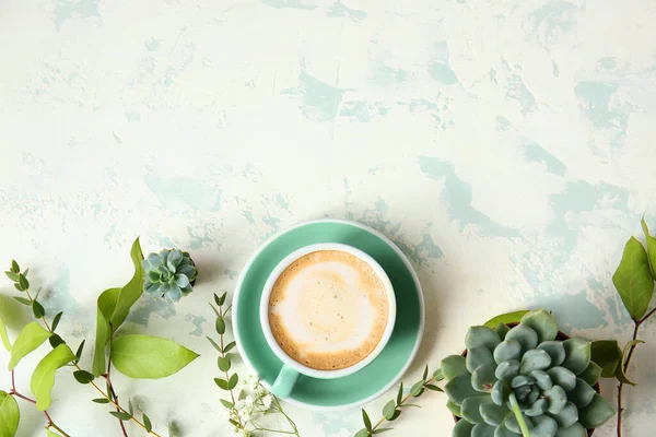 Cup of coffee and green plants on color background