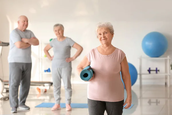 Elderly woman with yoga mat in gym