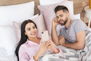 Evde yatağında cep telefonu olan genç bir çift.
