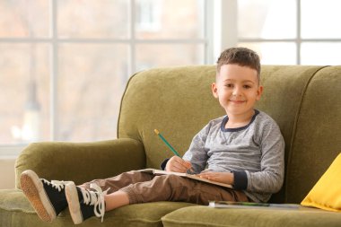 Evdeki kanepede oturan küçük sevimli çocuk.