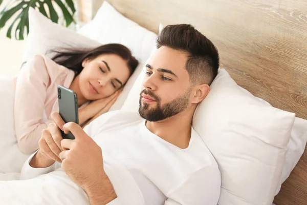Joven Usando Teléfono Móvil Mientras Esposa Duerme Cama — Foto de Stock