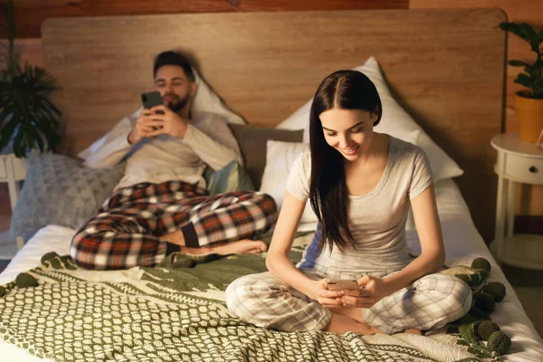 Young couple with mobile phones on bed at home