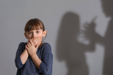 Gri arka planda kavga eden küçük bir kız ve ailesinin gölgesi.
