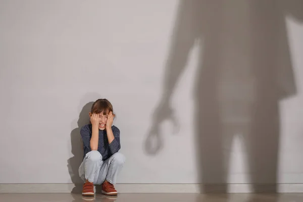 Shadow of father threatening his little daughter who is sitting on floor near grey wall