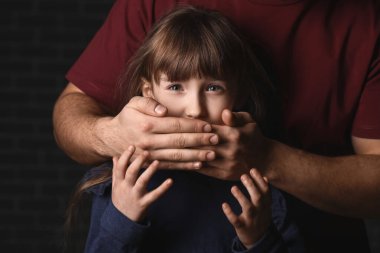 Baba, korkmuş küçük kızının ağzını karanlık arka planda kapatıyor. Aile içi şiddet kavramı
