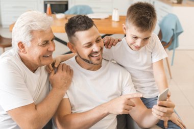 Babası ve oğluyla evde cep telefonu kullanan bir adam.