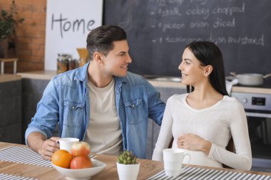 Genç hamile çift mutfakta çay içiyor.