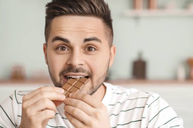 Yakışıklı genç adam mutfakta çikolata yiyor.
