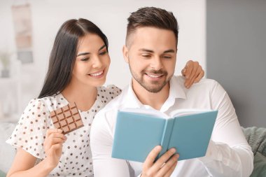 Genç adam kitap okurken kadınlar evde lezzetli çikolatalar yiyor.