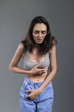 Gri arka planda iştahsızlığı olan genç bir kadın.