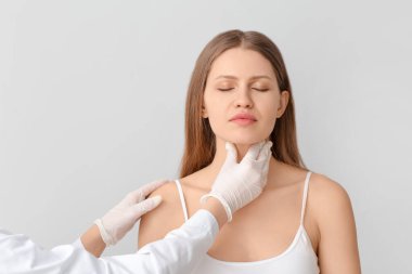 Endokrinolojist, genç bir kadının boğazını ışıkla inceliyor.