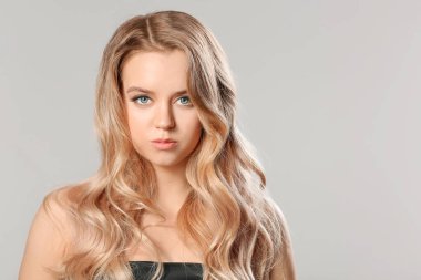 Gri arka planda güzel saçları olan genç bir sarışın.