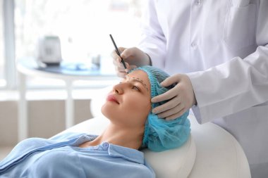 Plastik cerrah klinikte kadının yüzüne izler sürüyor.