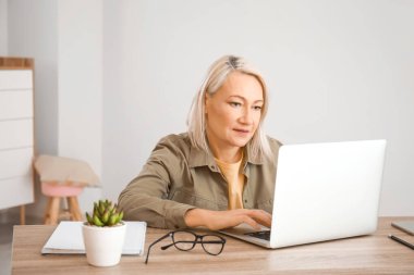 Evde online öğrenim için dizüstü bilgisayar kullanan olgun bir kadın