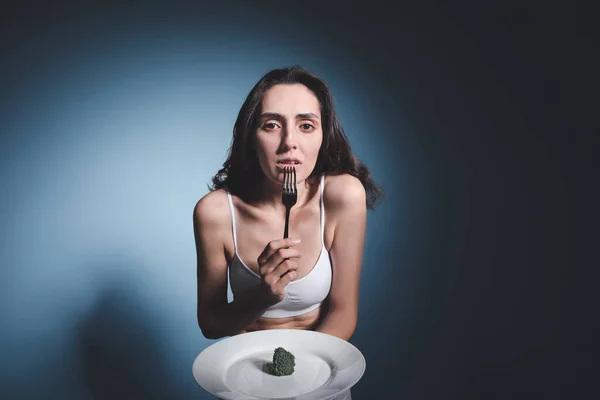 暗い背景にプレート上のブロッコリーと病気の女性 拒食症の概念 — ストック写真