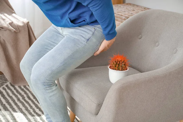 Young man near armchair with cactus at home. Hemorrhoids concept