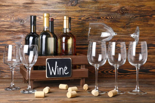 Box with bottles of wine and glasses on wooden background