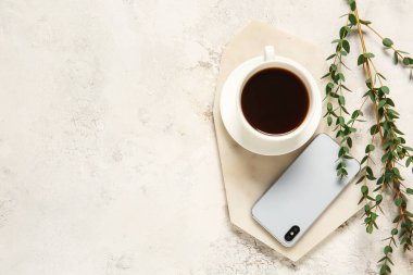 Bir fincan kahve, cep telefonu ve arka planda yeşil dallar.