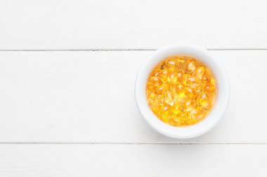 Beyaz ahşap arka planda balık yağı kapsülleri.