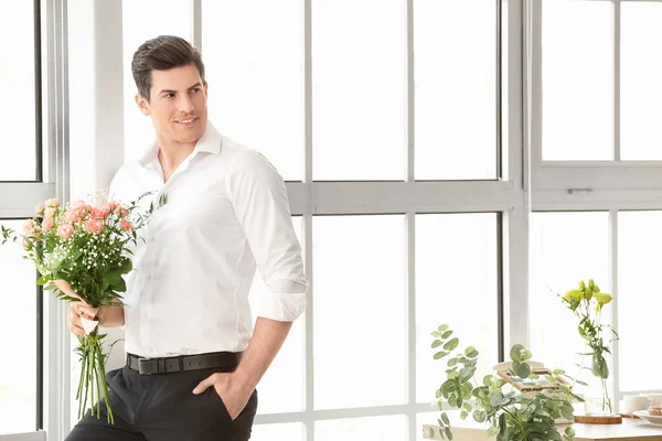 Handsome man with bouquet of flowers indoors