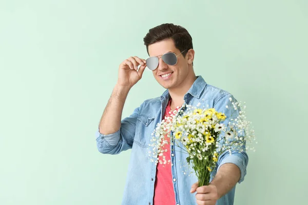 Handsome man with bouquet of flowers on color background