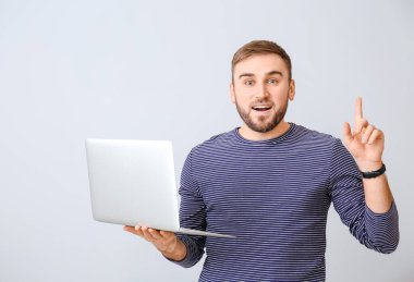 Dizüstü bilgisayarı olan erkek programcı ve ışık arka planında işaret parmağını kaldırdı
