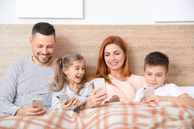 Evdeki yatak odasında cep telefonu olan mutlu bir aile.
