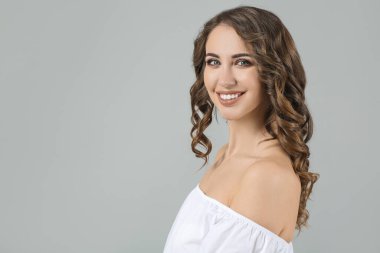 Gri arkaplanda kıvırcık saçlı güzel bir genç kadın.