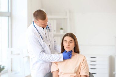 Endocrinologist examining throat of young woman in clinic clipart