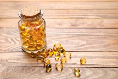 Ahşap zemin üzerinde balık yağı kapsülleri olan kavanoz.