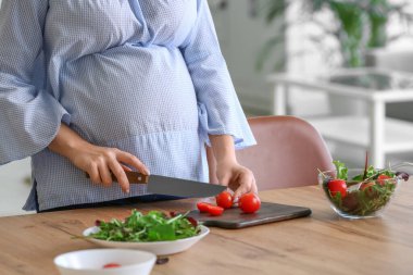 Güzel genç hamile kadın mutfakta yemek pişiriyor.