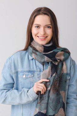 Gri arka planda şık bir eşarbı olan güzel bir genç kadın.