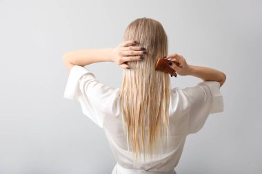 Saçlarını gri arka planda tarayan genç bir kadın.