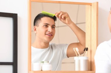 Evde saçını tarayan yakışıklı genç adam.