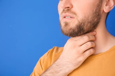 Genç adam tiroit bezini renk arkaplanında kontrol ediyor, yakın plan.