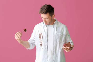 Kirli elbiseli sorunlu bir adam arka planda çikolatalı pasta yiyor.