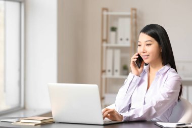 Ofiste telefonla konuşan Asyalı genç iş kadınının portresi.