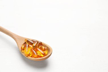 Beyaz ahşap arka planda balık yağı kapsüllü kaşık