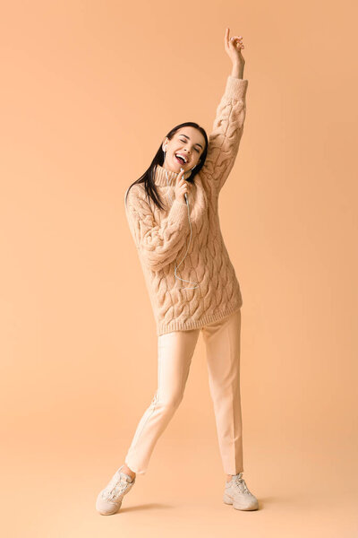 Beautiful young woman listening to music and dancing against color background