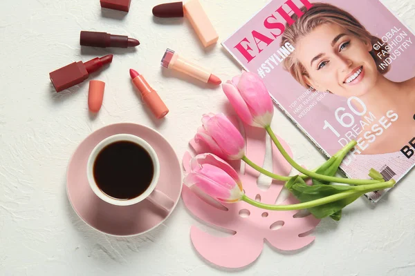 Cup of coffee, fashion magazine, flowers and cosmetics on light background