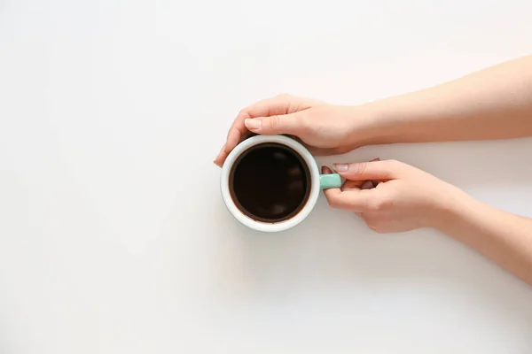 Female hands with cup of hot coffee on light background, top view