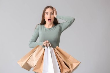 Gri arka planda alışveriş torbaları olan şaşırmış genç bir kadın.